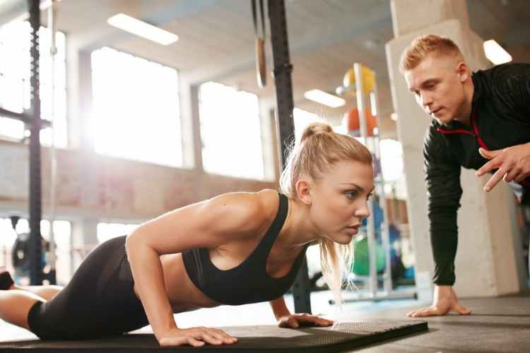 Female exercising with personal trainer at gym